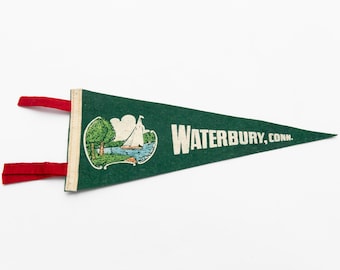 May include: A green pennant with the text "WATERBURY, CONN." in white. The pennant features a detailed illustration of a sailboat on a lake. Red fabric strips are attached to the pennant's left side.