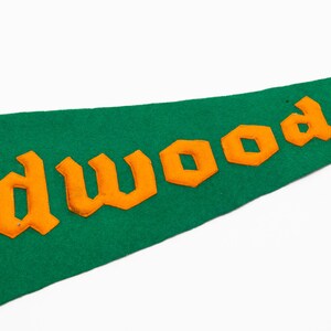 May include: Green felt pennant with orange lettering that reads "Wildwood N". The pennant is a classic shape, with a pointed end. The lettering is in a bold, blocky font.