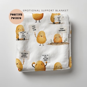 Peut inclure: Couverture blanche avec des illustrations de pommes de terre de dessins animés tenant des pancartes avec des messages positifs. La couverture porte les inscriptions "EMOTIONAL SUPPORT BLANKET" et "POSITIVE POTATO". Les pancartes disent "YOU GOT THIS", "YOU CAN DO HARD THINGS", et "IT'S OK TO FEEL ALL THE FEELS".