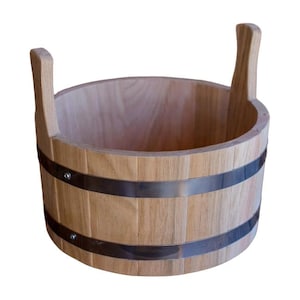 Może przedstawiać: Jasnobrązowe drewniane wiadro z dwoma zakrzywionymi uchwytami. Wiadro jest wzmocnione dwoma srebrnymi metalowymi obręczami. Widoczne jest usłojenie drewna, a wiadro ma naturalny, rustykalny wygląd.