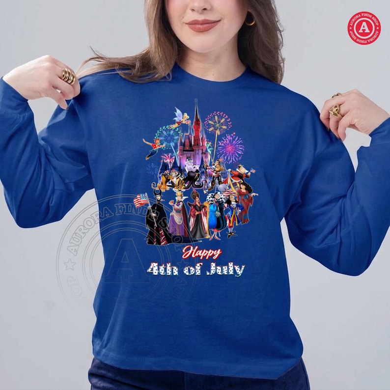 May include: A blue long-sleeve shirt featuring a colorful graphic of a castle, fireworks, and various characters. The text "Happy 4th of July" is displayed in red and white.