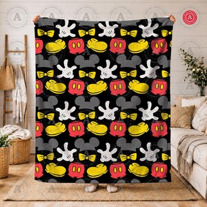 K&ouml;nnte beinhalten: Schwarze Decke mit einem sich wiederholenden Muster von Mickey Mouse-Elementen. Das Design umfasst wei&szlig;e Handschuhe, gelbe Fliegen, rote Shorts, gelbe Schuhe und graue Mauseohren. Die Decke wird von zwei H&auml;nden gehalten.