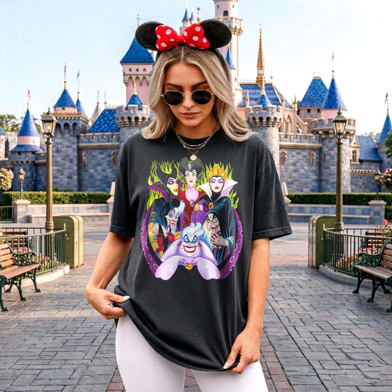 May include: Black t-shirt featuring a graphic of Disney villains, including Ursula, surrounded by green flames and purple tentacles. The design is centered on the shirt. The person is wearing a Minnie Mouse ear headband with a red bow and sunglasses.