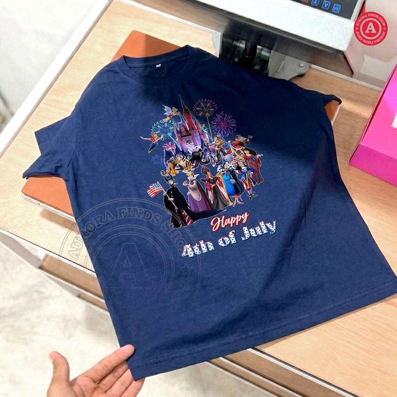 May include: Navy blue t-shirt featuring a colorful graphic of a castle, characters, and fireworks. The text "Happy 4th of July" is printed in white. The shirt is made of a soft material.