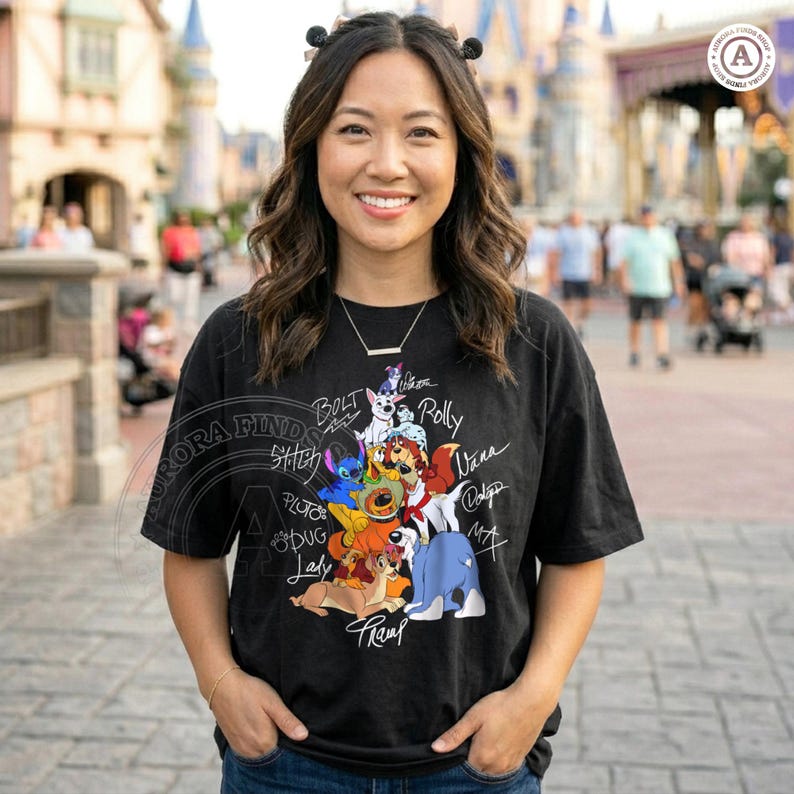 K&ouml;nnte beinhalten: Schwarzes T-Shirt mit einer bunten Grafik von Zeichentrickhunden, darunter Bolt, Stitch und Pluto, mit ihren Namen. Das Shirt hat einen Rundhalsausschnitt und kurze &Auml;rmel. Das Design enth&auml;lt den Text "Aurora Finds".