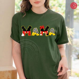 May include: Dark green t-shirt with the word "MAMA" in a playful design. The letters feature Mickey Mouse ears, red and yellow accents, and a checkered pattern, creating a fun and whimsical look.