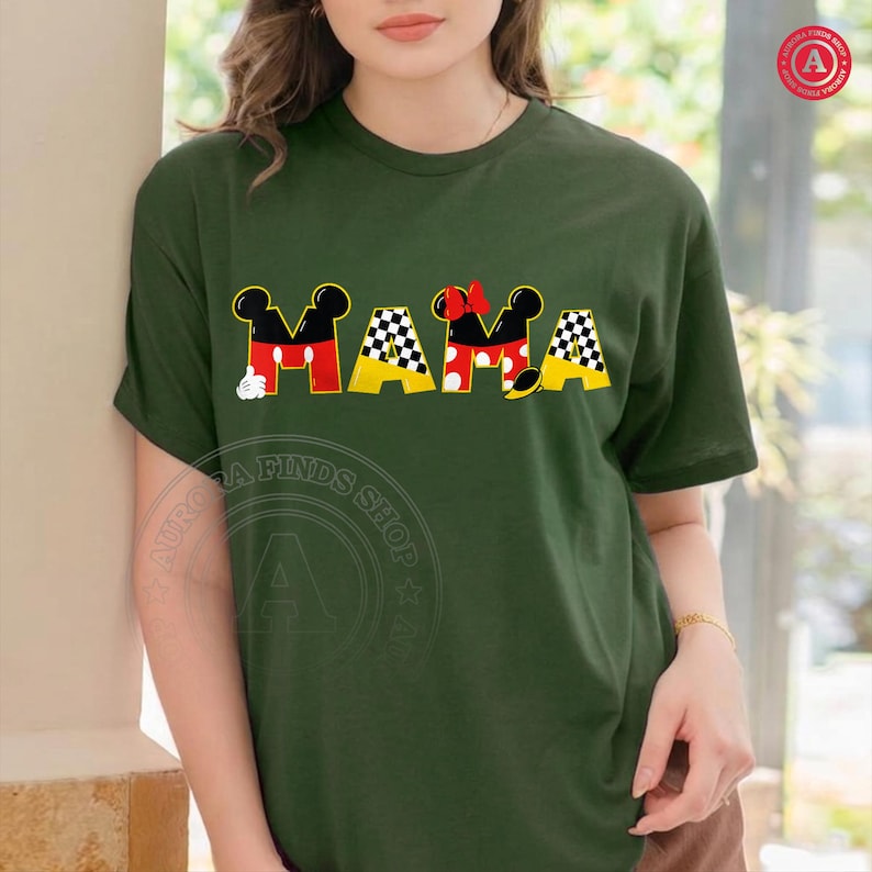 May include: Dark green t-shirt with the word "MAMA" in a playful design. The letters feature Mickey Mouse ears, red and yellow accents, and a checkered pattern, creating a fun and whimsical look.