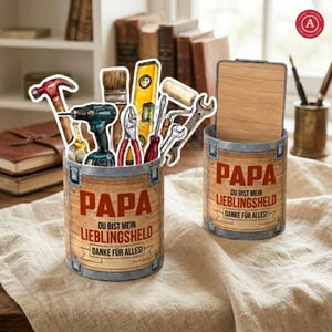 以下が含まれることがあります： 「PAPA」の文字とドイツ語のテキストが入った、木目調の容器が2つ。片方の容器には、ハンマー、ドリル、レンチなどの工具の切り抜きが入っています。もう片方の容器には木の蓋が付いています。テキストは「DU BIST MEIN LIEBLINGSHELD DANKE FÜR ALLES!」と書かれています。