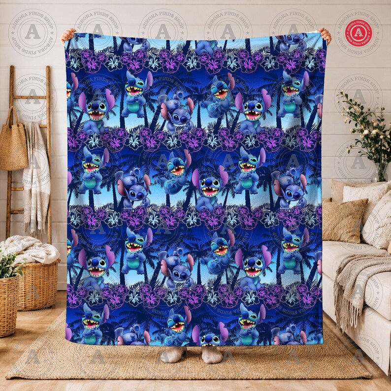 Puede incluir: Una manta azul con un patr&oacute;n repetido del personaje Stitch de Lilo & Stitch, palmeras y flores moradas. La manta tiene un fondo azul oscuro con el texto "AURORA FINDS SHOP" en un patr&oacute;n circular. La manta est&aacute; sujeta por una persona.