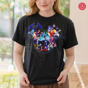 K&ouml;nnte beinhalten: Schwarzes T-Shirt mit einem farbenfrohen Design von Disney-B&ouml;sewichten, die in Form eines Mickey Mouse-Kopfes angeordnet sind. Das Design umfasst Charaktere wie Maleficent und Ursula. Das T-Shirt hat kurze &Auml;rmel und einen Rundhalsausschnitt.