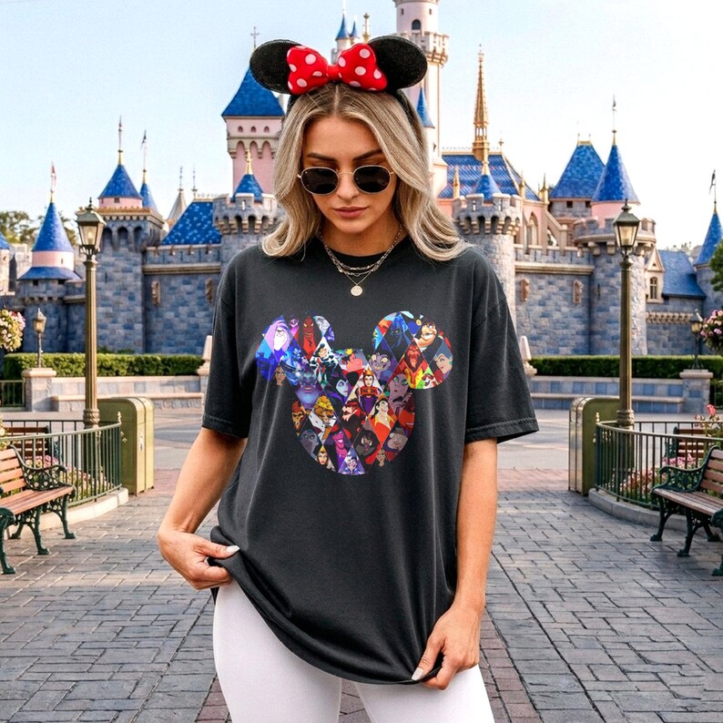 Puede incluir: Camiseta negra con un dise&ntilde;o de cabeza de Mickey Mouse lleno de villanos de Disney. La camiseta se usa con una diadema de orejas de Minnie Mouse con un lazo rojo de lunares. Un castillo es visible en el fondo.