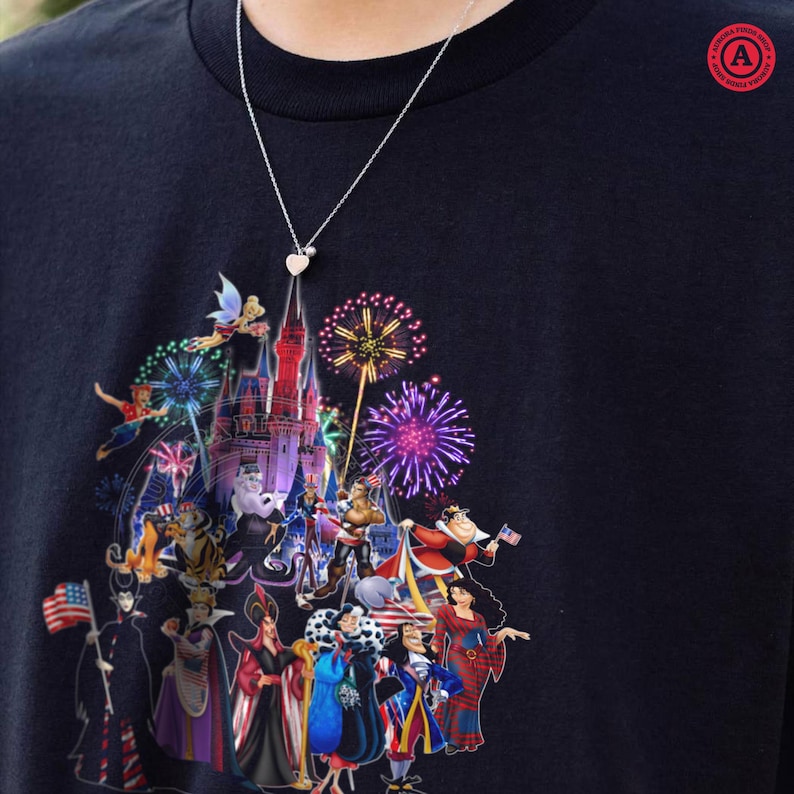 May include: Navy blue t-shirt featuring a colorful graphic of a castle, fireworks, and various cartoon characters. A silver necklace with a heart pendant is visible. The shirt has a round neck and short sleeves. The graphic includes characters from popular animated films.