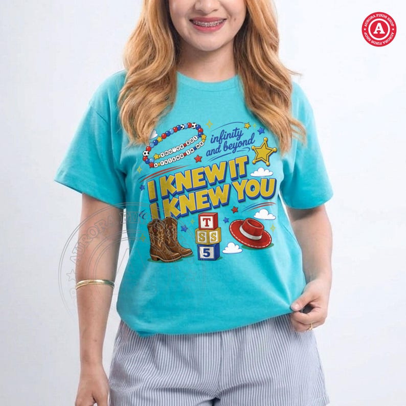 Puede incluir: Una camiseta de manga corta de color turquesa brillante con un estampado gr&aacute;fico que incluye el texto "I KNEW IT I KNEW YOU" y "infinity and beyond". El dise&ntilde;o muestra ilustraciones de botas vaqueras marrones, un sombrero rojo y bloques.