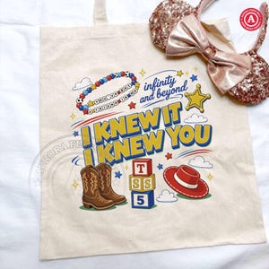 Puede incluir: Una bolsa de tela beige con un estampado gr&aacute;fico colorido que incluye el texto "I KNEW IT I KNEW YOU", "infinity and beyond" y "YOU'VE GOT A FRIEND IN ME". El dise&ntilde;o muestra botas vaqueras marrones, bloques de letras y un sombrero rojo.