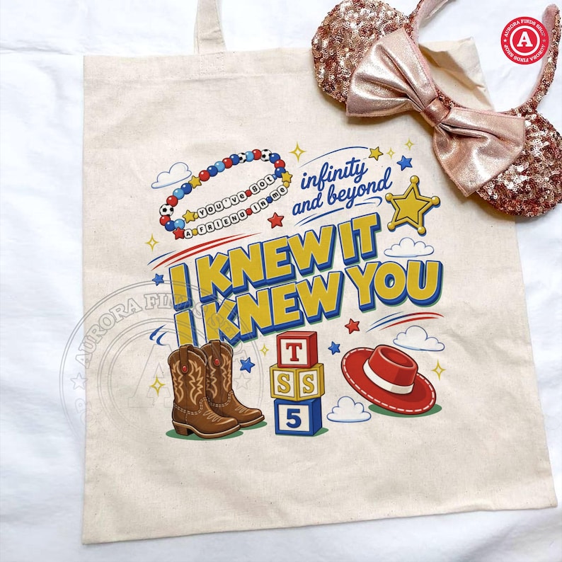 Puede incluir: Una bolsa de tela beige con un estampado gr&aacute;fico colorido que incluye el texto "I KNEW IT I KNEW YOU", "infinity and beyond" y "YOU'VE GOT A FRIEND IN ME". El dise&ntilde;o muestra botas vaqueras marrones, bloques de letras y un sombrero rojo.