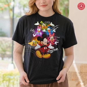 K&ouml;nnte beinhalten: Schwarzes T-Shirt mit einem farbenfrohen Aufdruck von Micky Maus und ihren Freunden, darunter Minnie Maus, Donald Duck und Goofy. Das Design enth&auml;lt Unterschriften der Charaktere und die Worte "Mickey Mouse".