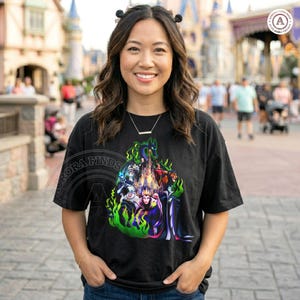 Puede incluir: Camiseta negra con un gr&aacute;fico colorido de villanos de Disney, incluyendo Mal&eacute;fica y la Reina Malvada, rodeados de llamas verdes y un castillo. La camiseta tiene el texto "Aurora Finds" en el lado izquierdo.