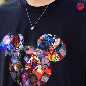 Puede incluir: Camiseta negra con un dise&ntilde;o de cabeza de Mickey Mouse lleno de im&aacute;genes coloridas de villanos de Disney. Se ve un collar plateado con un colgante de coraz&oacute;n. La camiseta tiene un logotipo redondo en la esquina superior derecha.