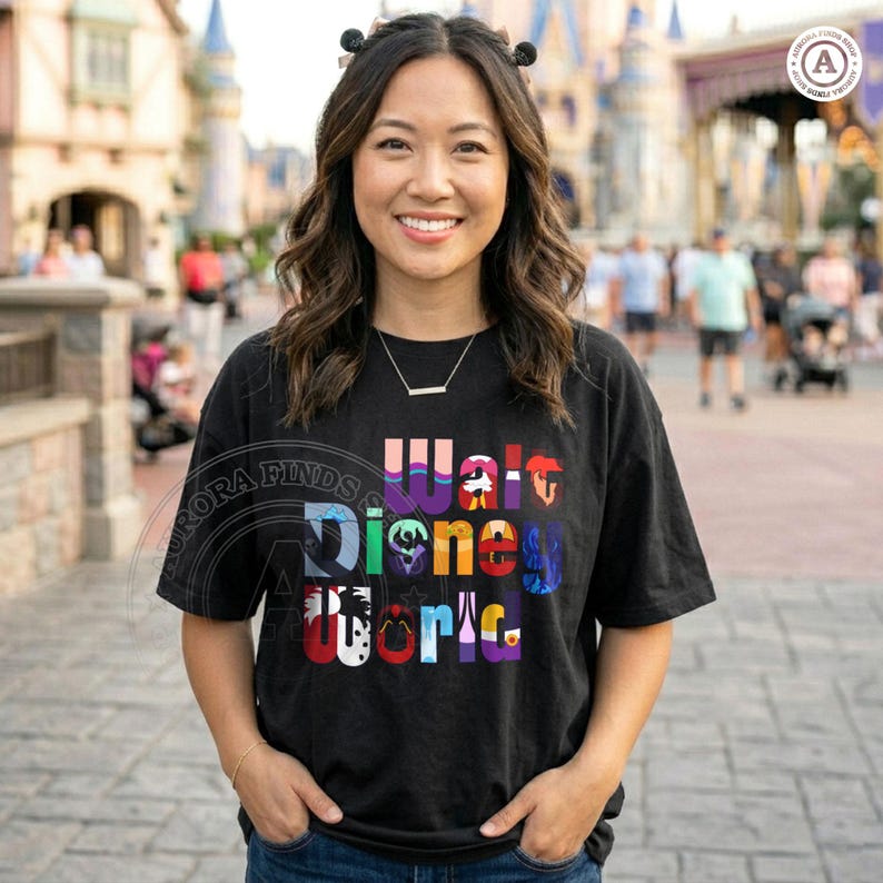 Puede incluir: Camiseta negra con las palabras "Walt Disney World" en letras coloridas y estilizadas. La camiseta la lleva una persona sonriendo frente a un parque tem&aacute;tico. La camiseta es de estilo casual.