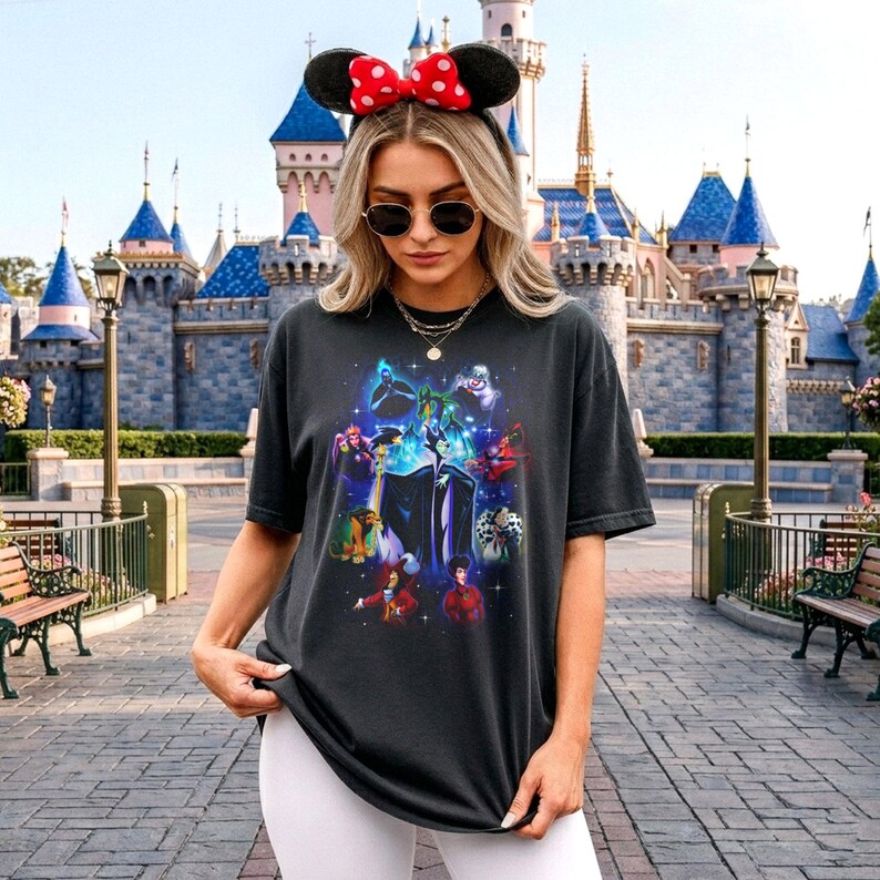 May include: Dark grey t-shirt with a vibrant graphic of Disney villains, including Maleficent and Cruella de Vil. The design features a crew neck and short sleeves. The shirt is a casual style.