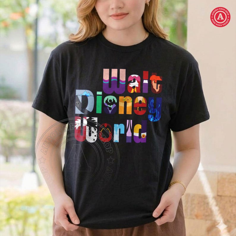 Puede incluir: Camiseta negra con las palabras "Walt Disney World" en letras coloridas y estilizadas. El dise&ntilde;o incorpora elementos de personajes de Disney dentro de las letras, creando una est&eacute;tica vibrante y l&uacute;dica. La camiseta es de manga corta.