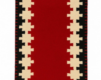 May include: Rectangular woven rug with a red center, bordered by a cream and black geometric pattern. The edges are finished with a red stitched border. The rug's design is symmetrical and visually striking.
