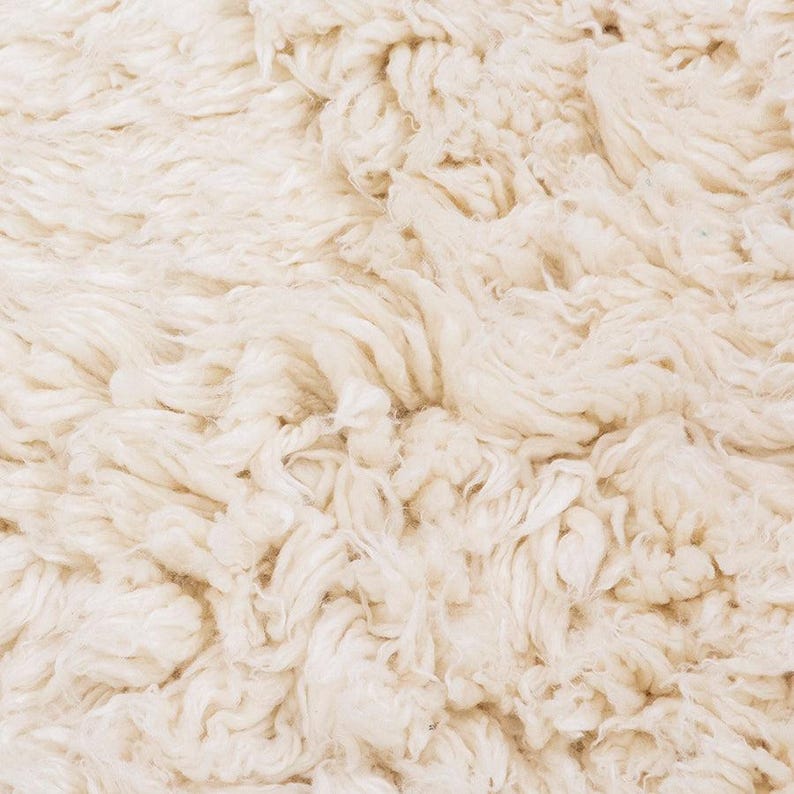 Pode incluir: Um tapete espesso de cor branco-sujo com uma textura de pelo alto e felpudo. A superf&iacute;cie consiste em fibras de fio torcidas e densamente compactadas que criam uma apar&ecirc;ncia macia, irregular e volumosa em todo o revestimento de piso.