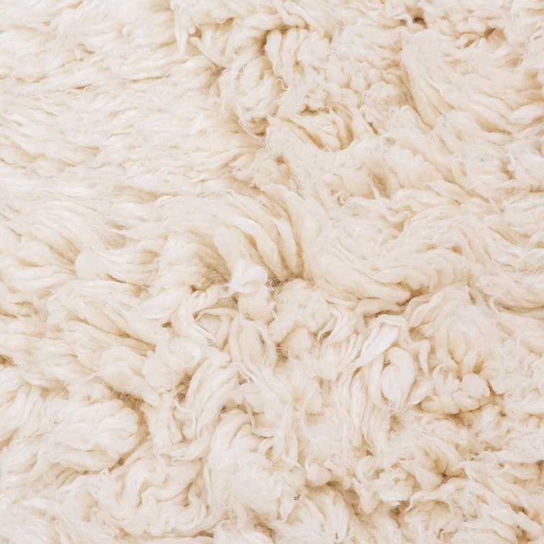 Pode incluir: Um tapete espesso de cor branco-sujo com uma textura de pelo alto e felpudo. A superf&iacute;cie consiste em fibras de fio torcidas e densamente compactadas que criam uma apar&ecirc;ncia macia, irregular e volumosa em todo o revestimento de piso.
