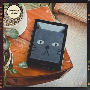 Könnte beinhalten: Ein schwarzer Kindle E-Reader mit einer grauen Katzenillustration auf dem Bildschirm. Der Text "Made for Kindle" ist in der oberen linken Ecke des Bildes sichtbar. Der E-Reader liegt auf einer Holzoberfläche.