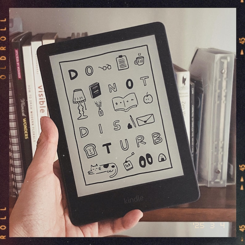May include: A black and white Kindle e-reader displaying a digital illustration of the phrase "Do Not Disturb" with various icons and doodles. The Kindle is on a bookshelf with other books.
