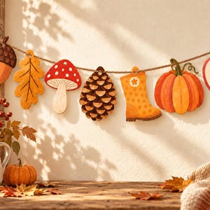 Op de afbeelding: Een decoratieve slinger met houten uitsparingen van een eikel, een geel blad, een rood-witte paddenstoel, een dennenappel, een oranje regenlaars, een pompoen en een doorgesneden appel, allemaal aan een touw van natuurlijke vezels geregen.