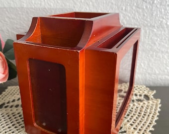 May include: A wooden desk organizer with a rich, reddish-brown finish. The organizer has multiple compartments, including a rectangular opening and a slot for pens or pencils. It sits on a cream-colored, lace doily.