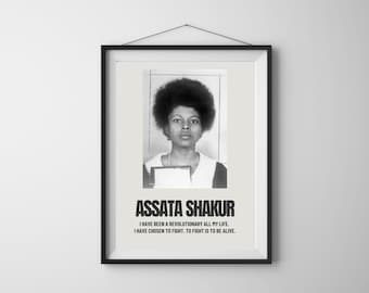 May include: Framed black and white print featuring a portrait of Assata Shakur. The print includes the text "ASSATA SHAKUR" and a quote about her revolutionary life. The framed print is hanging on a white wall.