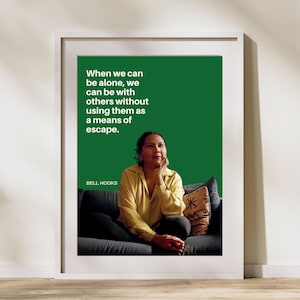 May include: A green poster with a quote by Bell Hooks that reads "When we can be alone, we can be with others without using them as a means of escape." A woman is sitting on a couch in the background.