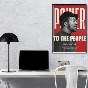 Fred Hampton print displayed on a workspace desk with a lamp and laptop. A bold, thought-provoking digital print for modern office and study spaces.