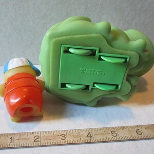 Puede incluir: Un juego de juguetes Playskool vintage con una peque&ntilde;a figura naranja y amarilla con una gorra azul y blanca, y una gran estructura rodante verde. El juego de juguetes es de pl&aacute;stico.