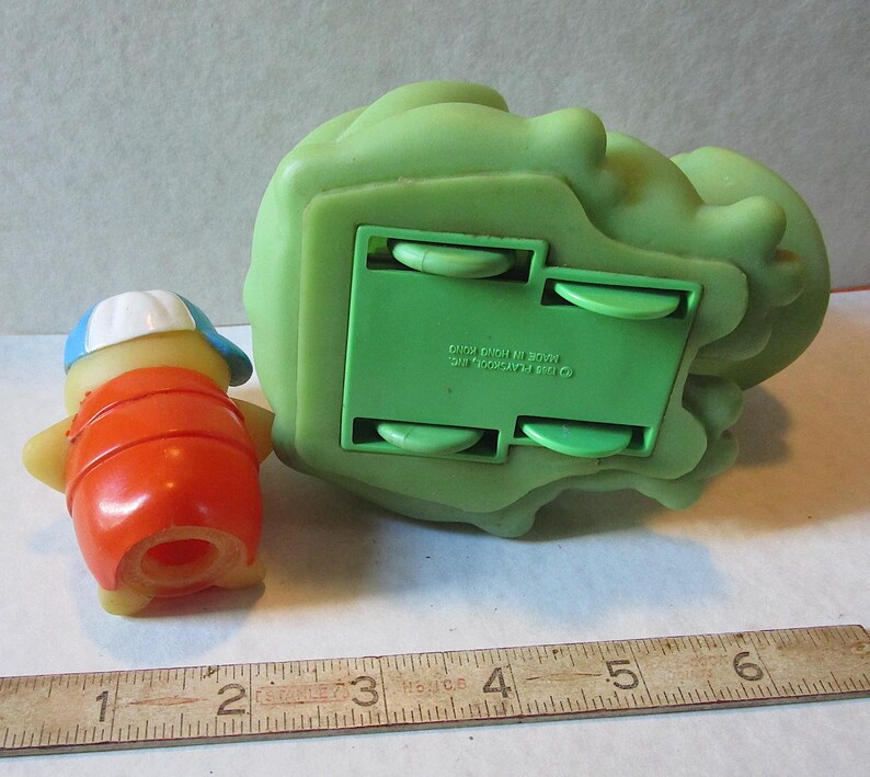 Puede incluir: Un juego de juguetes Playskool vintage con una peque&ntilde;a figura naranja y amarilla con una gorra azul y blanca, y una gran estructura rodante verde. El juego de juguetes es de pl&aacute;stico.