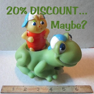 Puede incluir: Un juguete vintage que presenta una figura amarilla con forma de insecto con una parte superior roja y una gorra azul montada en una rana verde. El texto "20% DISCOUNT... Maybe?" est&aacute; escrito en verde encima de las figuras. Una regla est&aacute; en la parte inferior.