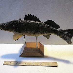 May include: A wooden carved fish model on a wooden stand. The fish is painted black and brown with a black fin. The fish is about 10 inches long.