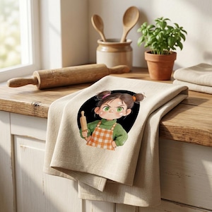 May include: Beige kitchen towel featuring a cartoon illustration of a girl holding a rolling pin, set against a black circle. The girl wears a green sweater and orange checkered apron. A rolling pin, wooden spoons, and a potted plant are in the background.