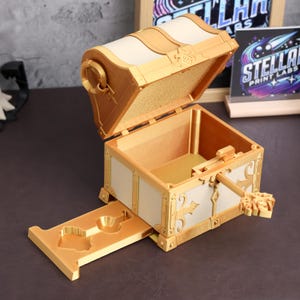 May include: A gold treasure chest with a white interior and a keyhole. The chest is open and has a drawer that slides out. The drawer has a keyhole and a small key.