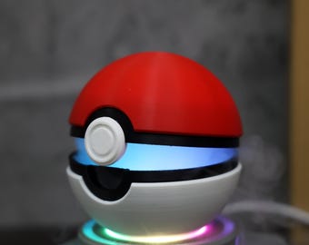 May include: A red and white Poke Ball shaped humidifier with a blue light ring around the middle. The humidifier is sitting on a circular base with a rainbow light effect.