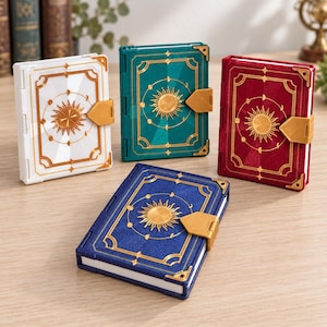 May include: Four rectangular notebooks with white, teal, red, and blue covers. Each notebook features a gold-colored sun and moon phase emblem on the front, gold corner accents, and a gold-colored latch closure on the right side of the cover.