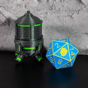 May include: A 3D-printed black container with green accents, featuring a cylindrical shape and a rounded top. Beside it is a blue and yellow 20-sided die. The objects are on a black surface.