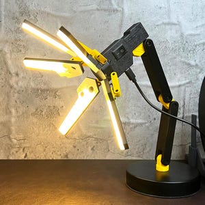 May include: A black and yellow articulated desk lamp with four adjustable LED lights. The lamp has a USB charging port and an on/off switch.