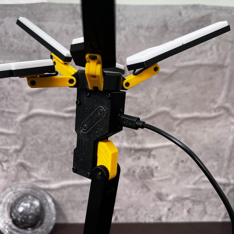 The Death Stranding inspired folding LED lamp is a stylish and practical addition to any space. With its futuristic design, this lamp features an adjustable structure that can be posed in various ways to suit your lighting needs. Made with high-quality PLA material, this 3D printed lamp showcases durability and attention to detail. The unique color combination of yellow, black, and metallic silver ties back to the Bridges organization seen in the Death Stranding game