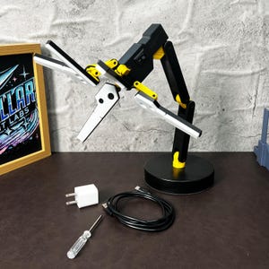 Designed to mirror the futuristic technology seen in Death Stranding, this 3D printed folding LED lamp brings a touch of sci-fi to any space. The lamp's adjustable arms and joints provide the flexibility to control the lighting angle and direction, while its compact, foldable design makes it perfect for on-the-go use or easy storage. Whether used for reading, ambient lighting, or as a decorative piece, this lamp is sure to impress. The warm LED light provides a comfortable glow