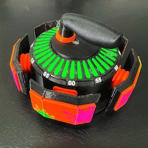 May include: A black and orange timer with a green and black dial. The timer has a handle and several orange and pink panels. The dial is marked with numbers from 00 to 55. The timer is designed with a modern aesthetic.