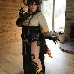 May include: A detailed cosplay costume featuring a horned headpiece, black gloves with claw-like extensions, and a long black and cream-colored dress. The costume includes gold accents, a decorative belt, and patterned leggings. The overall aesthetic is fantasy-inspired.