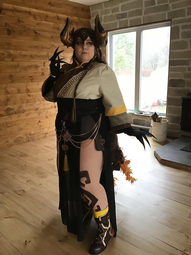 May include: A detailed cosplay costume featuring a horned headpiece, black gloves with claw-like extensions, and a long black and cream-colored dress. The costume includes gold accents, a decorative belt, and patterned leggings. The overall aesthetic is fantasy-inspired.